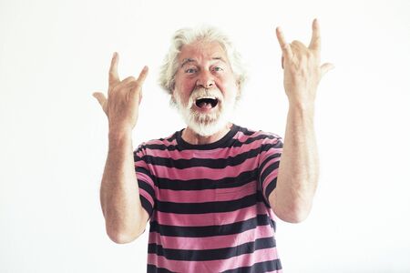 Senior people caucasian man do rock'n roll signs with crazy funny expression portrait - happy mature retired lifestyle have fun with no limit age - white background studio shotの写真素材