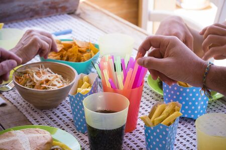 close up of hands taking chips and food of the table in a happy party in a house - family together celebrating together - junk and unhealthy food like hamburgerの写真素材