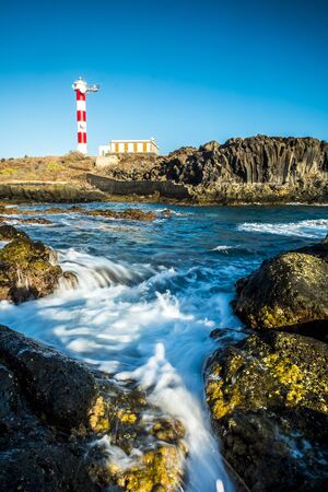 Beautiful scenic landscape with classic lighthouse on the coast and blue ocen and sky in background - concept of travel and vacation for tourism - wave and rocksの写真素材