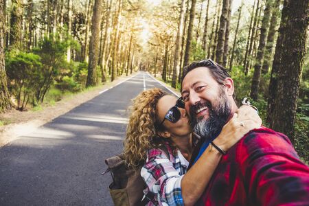 Travel people outdoor concept with happy couple caucasian man and woman hug and kiss  with love - relationship and vacation on mountain forest for cheerful adults - enjoying and happiness lifestyle for hipstersの写真素材