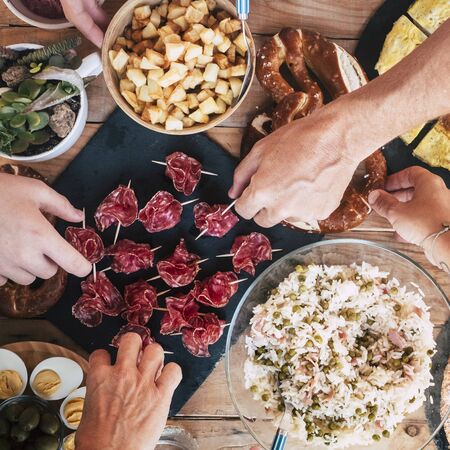 Close up vertical view of table full of fresh tasty food and hands picking and people eating - concept of friendship and leisure activity together - background with. wooden tableの写真素材