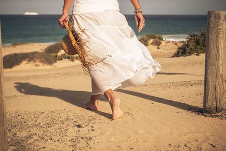 Warm summer holiday vacation travel in beach paradise resort concept with beautiful elegant woman viewed from back salking barefoot on the sand enjoying the sea water and outdoorの写真素材