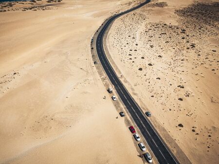 Aerial view of black asphalt road in the middle of the beach - desert around and concept of travel and vacation.   tropical scenic place - transport and parked cars in  wild landscapeの写真素材