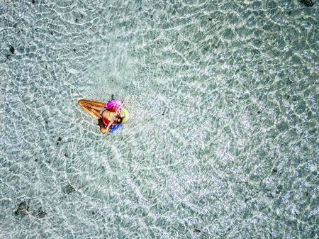 Aerial view. of beautiful caucasian people adult woman tourist lay dawn and relaxing on a trendy coloured lilo with transparent and clean tropical sea water around - concept of summer vacation and happinessの写真素材