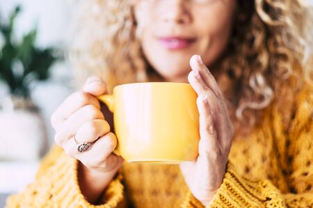 Close up on cup with tea or coffe drink inside and beautiful defocused woman in background - concept of relax and healthy lifestyle with nice people - yellow colors moodの写真素材