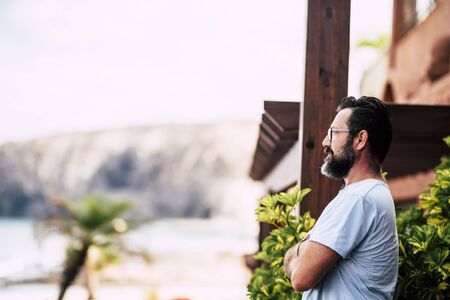 Beard adult caucasian standing man looking outside at home - concept of security and outdoor space - people with glasses portraitの写真素材