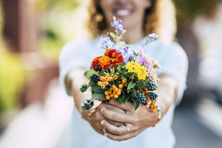 Close up of flowers bouquet and cheerful caucasian woman defocused in background - colors and earth planet environment respect concept - people and nature love concept - gift or present to youの写真素材