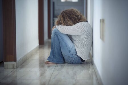Loneliness and depression disease concept with sad woman hug herself sit down on the floor a home alone - protection needed and violence against woman and wife imageの写真素材