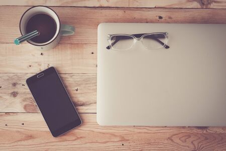 Wooden hipster modern office desk table with laptop, coffee, smartphone and eyeglasses - flat layer photo for modern technology work concept - workstation at home with many devicesの写真素材