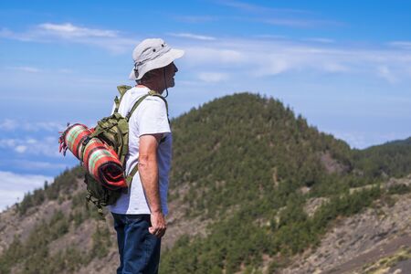 Active senior old man caucasian people enjoying travel outdoor lifestyle - mature backpacker looking the panorama - green mountains and blue sky in backgroundの写真素材