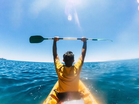 Rear view of tourist man giving up arms enjoying the  kayak excursion in the blue ocean water - concept of happiness for travel and leisure activity outdoor during summer holiday vacationの写真素材