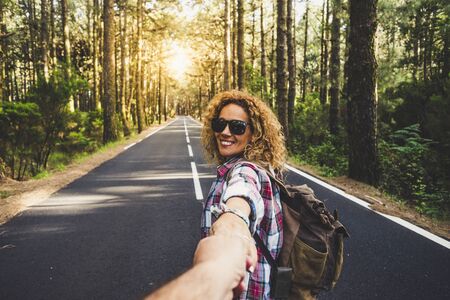 Couple travelers Man and Woman follow holding hands at long way road forest landscape and sun on background Love and Travel happy emotions Lifestyle concept. People traveling active adventure vacationsの写真素材