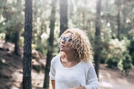 Beauiful blonde curly woman enjoy the outdoor leisure activity in the forest - People in the wood trees nature with defocused background and   sun in backlightの写真素材