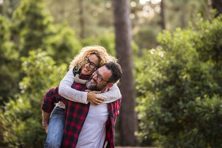 Happy couple of adult people caucasian man and woman have fun together in outdoor leisure activity in the nature- environment and love or forest concept with playful and youthful hipsters travelerの写真素材