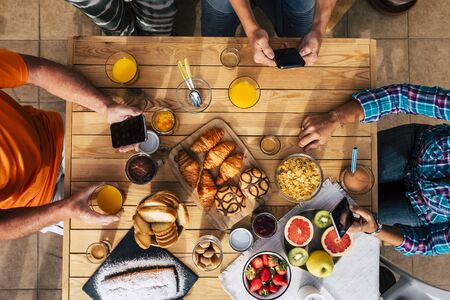 Breakfast time in vertical top view with family of friends eating together - technology mobile internet social network addiction for caucasian people using cellular at the table with friendsの写真素材