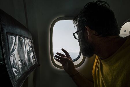 Beard hipster modern man travel on airplane looking outside the window -  concept of people fly and use flight transport to move and discover the world or work in new placesの写真素材