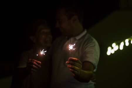 Celebration and happiness concept with dark couple with sparkler fire by night - new year eve motivational image - romantic and romance love atmosphere with red colors and feelingの写真素材