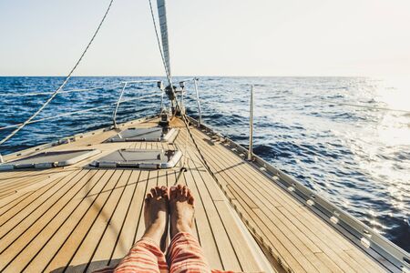 Close up of tourist woman caucasian feet lay down and relaxing enjoying a sail boat trip with ocean around and horizon in background - concept of luxury happy vacation for peopleの写真素材