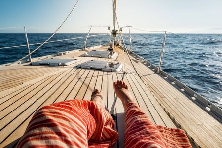 Close up of tourist woman caucasian feet lay down and relaxing enjoying a sail boat trip with ocean around and horizon in background - concept of luxury happy vacation for peopleの写真素材
