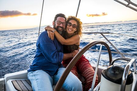 Happy people caucasian adult couple enjoy the sail boat trip on summer holiday vacation - outdoor leisure activity with ocean and sunset in. background - sailing with love and romanceの写真素材