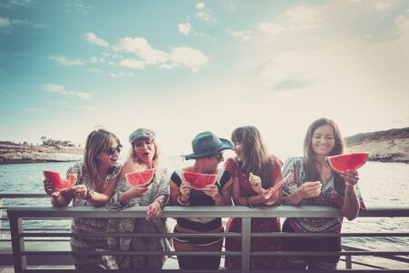 Group of people young cheerful happy women celebrate and enjoy friendship together outdoor with blue sky and ocean in background eating summer fresh watermelonの写真素材