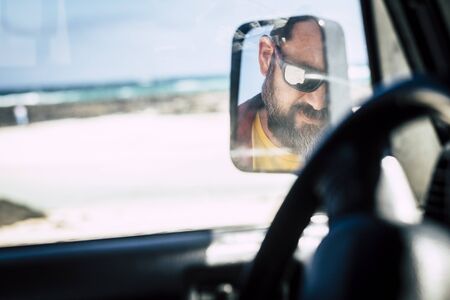 Caucasian man face with sunglasses viewed in the mirror of the car - alternative people portrait - travel vehicle conceptの写真素材