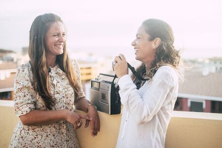 Couple of women happy friends smile and have fun laughing a lot together outdoor on the terrace at home - beautiful city view and nice pretty people together in friendshipの写真素材