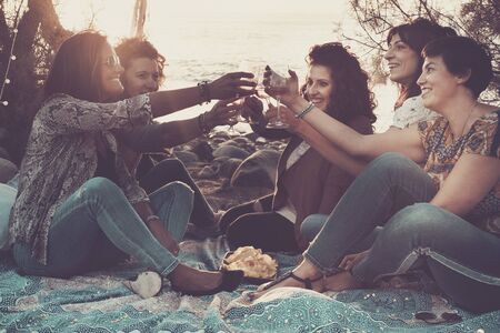 Group of happy cheerful adult caucasian women celebrate with wine together during the sunset at the beach - people on vacation and outdoor lifestyle concept with friendship and young ladiesの写真素材