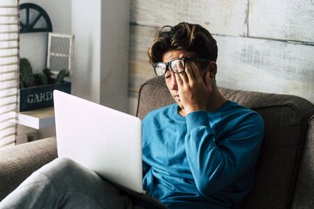 Stressed student at home studying with personal laptop computer - tired teenager for school work -internet. addiction for game or job search concept - indoor technology activityの写真素材