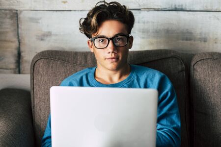 Portrait of handsome caucasian people teenager working with personal laptop computer at home sitting on the sofa - concept of student for high school or graduate or job search with modern technologyの写真素材