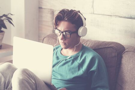 Young student at home with modern laptop computer and headphone studying with internet cnnection - handsome boy sitting on the sofa with technology indoorの写真素材