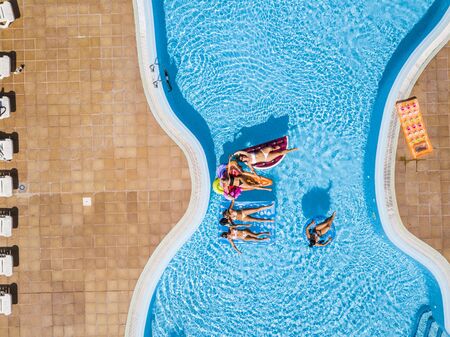 Top high aerial view of group of female caucasian people enjoying the pool with coloured trendy lilos mattress - summer holiday vacation hotel concept with blue water and relaxed funny girlsの写真素材