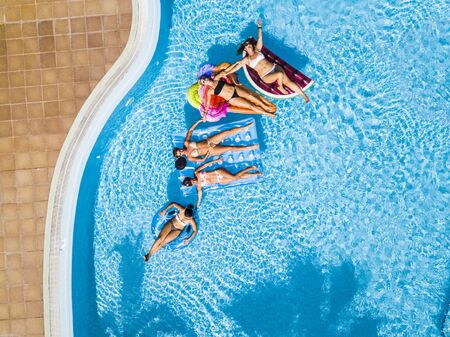 Coloured aerial background with group of friends woman caucasian people enjoying the summer holiday vacation at the blue water pool with trendy inflatable mattress lilos together with fun and happinessの写真素材