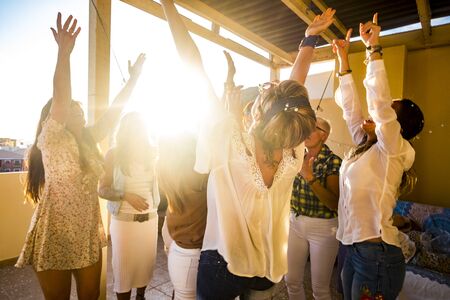 Active happy group of young free caucasian people woman celebrate and dance all together with friendship - sunset in backlight for party at home concept - Happiness for groupの写真素材