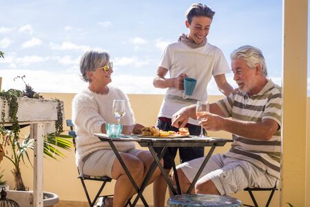 grandfathers adult mature and teenager nephew enjoy outdoor in the terrace some leisure with food and drinks. ocean and city view, vacation sunny day nice weather concept and background. happy people family togetherの写真素材