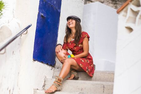 Trendy cheerful caucasian young lady sit down on outdoor white stairs and laugh a lot alone - people having fun and red dress fahsion woman portraitの写真素材
