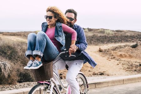 Cheerful caucasian people having fun together in friendship and relationship - adults couple laugh a lot both on a bike enjoying the outdoor leisure activityの写真素材