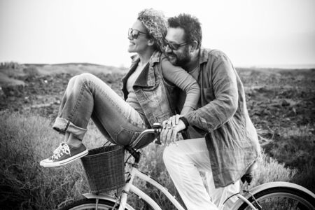 happy adult caucasian, couple having fun with bicycle in outdoor leisure activity. concept of active playful people with bike during vacation - everyday joy lifestyle withouth age limitation -の写真素材