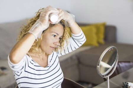 Home made hair dye at home for beauty young caucasian woman looking at the mirror - stay at home concept for coronavirus emergency worldwide pandemic contagionの写真素材