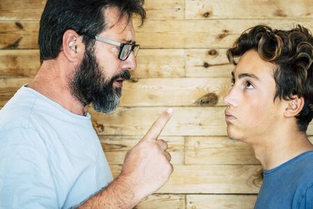 Adult caucasian man father telling out her teenager son at home - family portrait and education concept - generations and parentship - wooden backgroundの写真素材