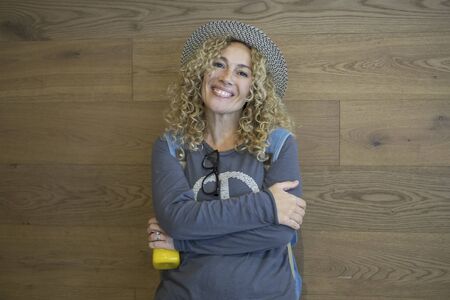 Cheerful caucasian adult woman pose for a standing portrait with wooden wall design in background -  concept of happy people and travel backpack lifestyle vacationの写真素材