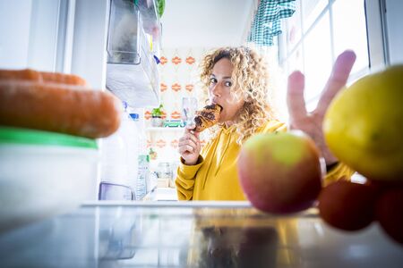 Alternaive inside view of Beautiful hungry adult woman eat tasty croissant with chocolate and open the fridge to take off some food -  concept of coronavirus covid-19 lockdown quarantine peopleの写真素材