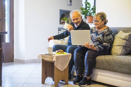 Retired senior people at home enjoying and use technology laptop computer during coronavirus lockdown quarantine time - elderly lifestyle with internet connectionの写真素材