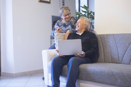 Retired senior people at home enjoying and use technology laptop computer during coronavirus lockdown quarantine time - elderly lifestyle with internet connectionの写真素材