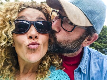 Adult caucasian couple portrait with park and nature in background - love and kiss outdoor leisure activity for beautiful woman and man together in funny leisure activityの写真素材