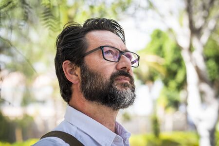 Handsome adult mature man with eyeglasses look and think in a portrait with green defocused background - professional people concept with trendy eyewear and beardの写真素材