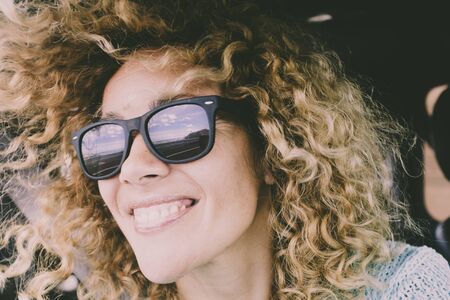 Close portrait of beautiful young adult caucasian cheerful happy woman smile and look at the road reflected on sunglasses during a car travelの写真素材