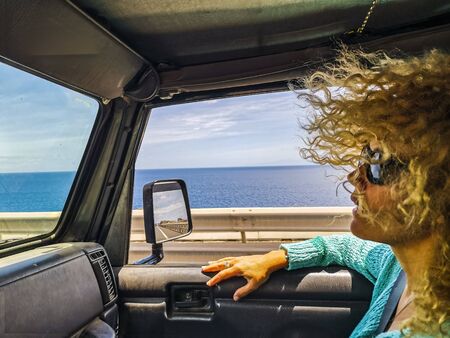 Concept of car travel with beautiful adult passenger woman enjoy the trip - ocean and blue sky view outside the window - concept of tourism and vacation transportの写真素材