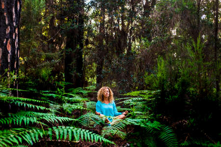 Beautiful adult lady do mindfulness exercises and yoga m editation sit down in the silence of the green nature forest - people enjoying alternative lifestyle and wood in tropical placeの写真素材