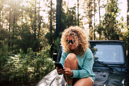 Beautiful free adult woman sit down on the car nose and use mobile phone technology connection in...